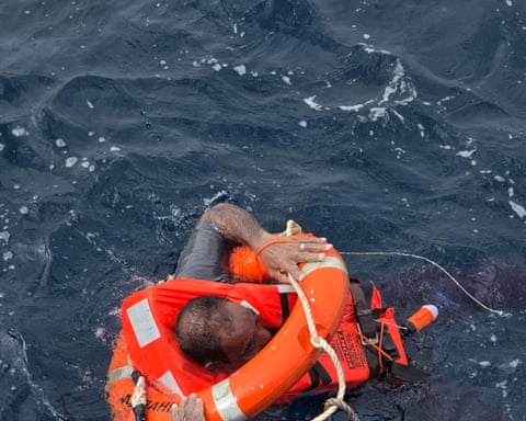 Man in a lifejacket with a flotation aid, holding on to a rope