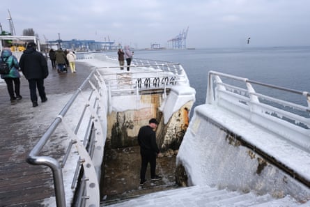 People walk along a snowy embankment with derricks in the distance