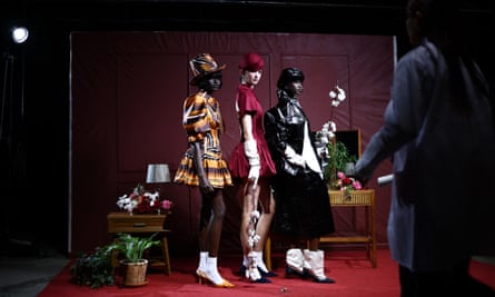 A trio of female models stand in a line showing off fashionable clothes in front of a red background