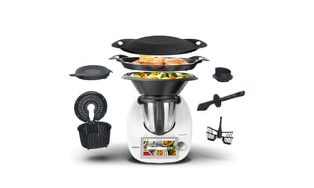 A silver, black and white Vorwerk Thermomix TM6 surrounded by black attachments, two of which have food in them