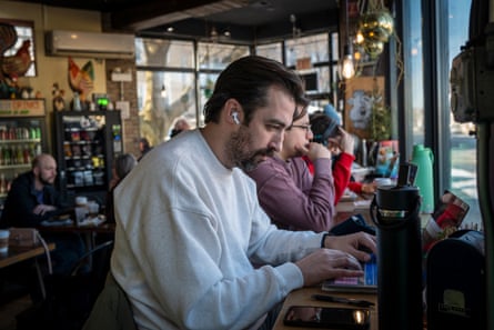 A man wearing earpods uses a laptop as he sits in a cafe.