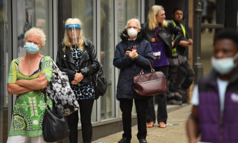 People wear PPE facemasks and visors as they queue to enter a bank in Leeds, UK.