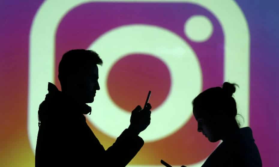 Silhouettes of models are seen next to a screen projection of Instagram logo.