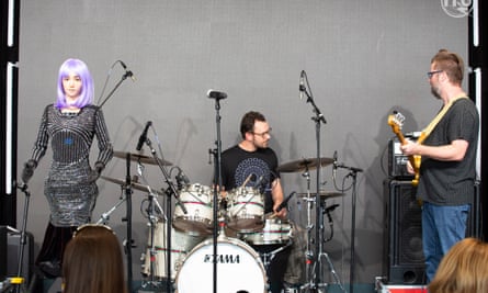 Desdêmona, uma humanóide estrela do rock de cabelos roxos, se apresenta no palco com a banda de apoio Jam Galaxy.