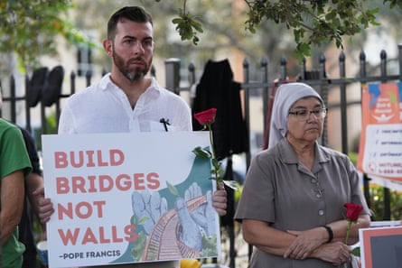 A man holds a sign saying ‘Build Bridges Not Walls’ next to a nun