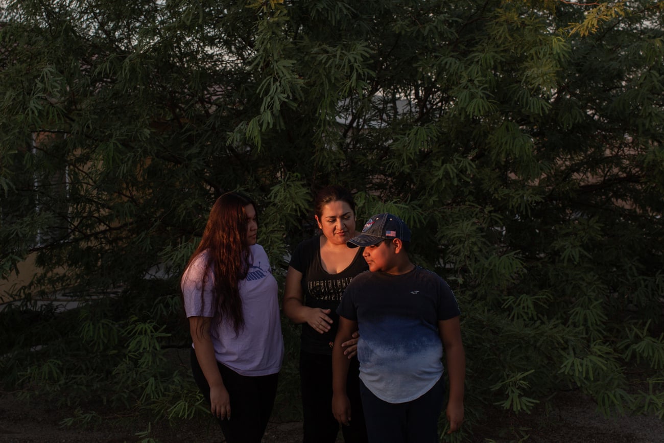 Nancy del Castillo stands with her daughter and son in the shadows of a large tree.