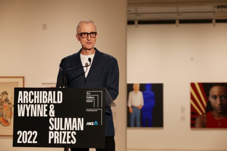 Nicholas Harding stands at a podium in an art gallery, a sign on the podium says Archibald, Wynne & Sulman Prizes 2022