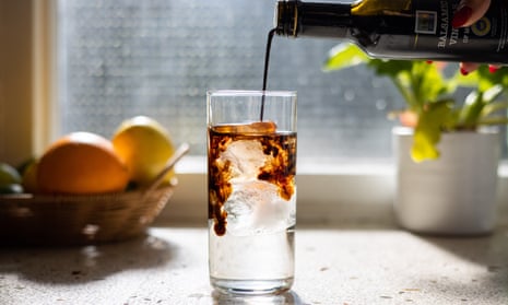Balsamic vinegar being poured into a glass of soda water and ice.