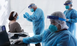 Workers prepare to test a woman for Covid at a free mobile test clinic set up outside Walker Temple AME Church in South Los Angeles in July.