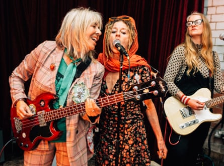 Three women, one with a bass guitar, one with an electric guitar, one singing into the microphone, all very engaged