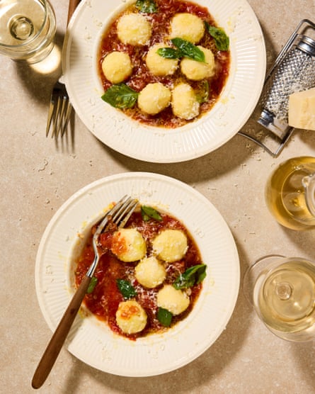 Two plates of gnudi with tomato sauce with cutlery and glasses