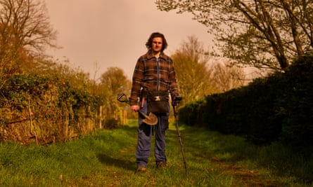 Tom Lucking in a lumberjack shirt and boots, holding a spade and metal detector