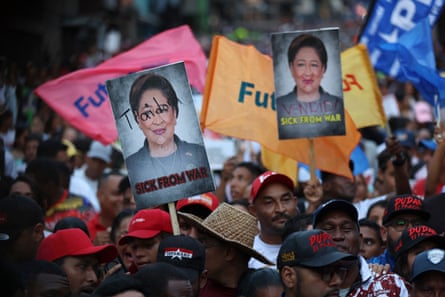 A crowd of people, many wearing branded caps and holding placards and banners