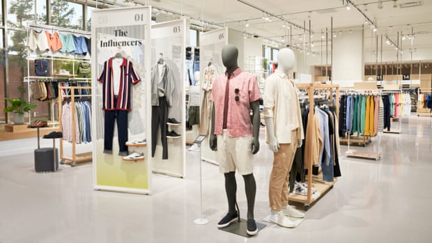 Clothes are displayed on racks and mannequins inside a white, brightly lit clothing store.