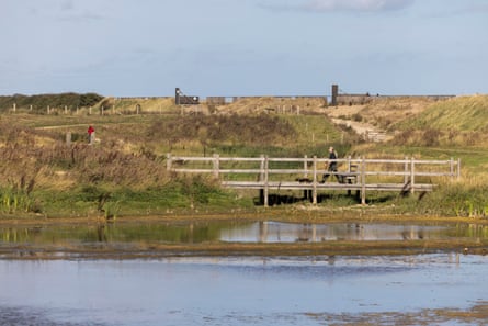 A woman with blond, long har walks across a bridge in a nature reserve