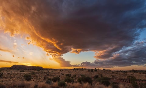 Uma enorme pluma de nuvens de tempestade paira sobre uma paisagem árida ao pôr do sol
