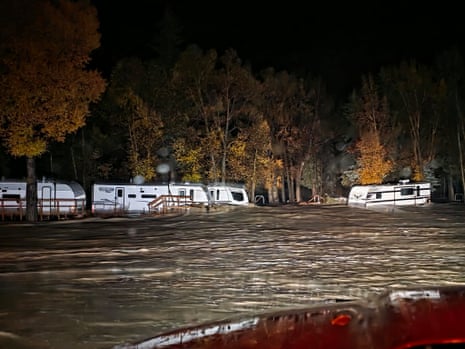 Floodwaters surround RV trailers at a campground at night, illuminated by bright light