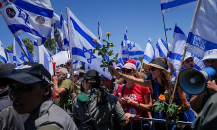 A large group of people at a barricade waving Israeli flags on a sunny day