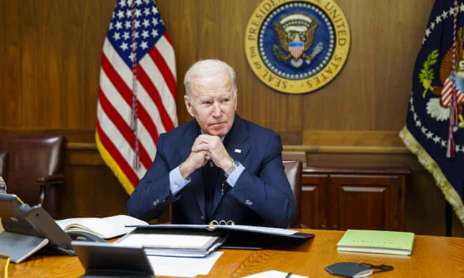 President Biden sitting at his desk with US flag and presidential insignia