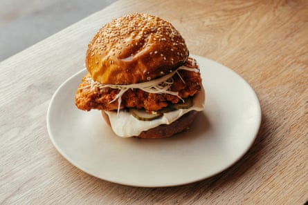 A fried chicken sandwich with pickles, slaw and sauce on a sesame bun, plated