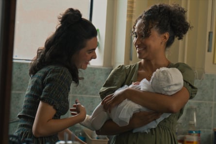 Kira is holding a baby, whom Lil is admiring, in a cloakroom