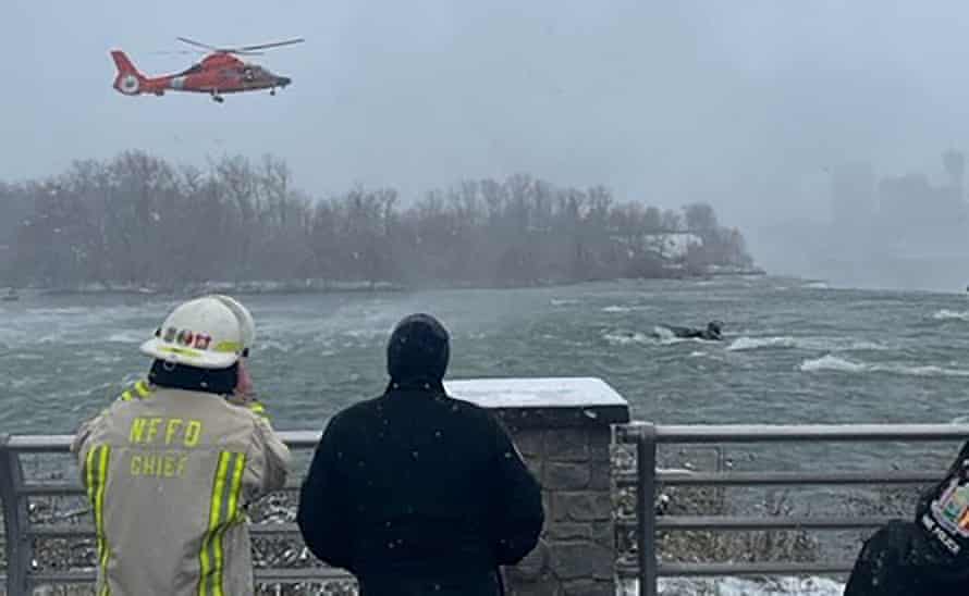 A US Coast Guard helicopter hovers over a vehicle submerged in the frigid water near the edge of Niagara Falls.