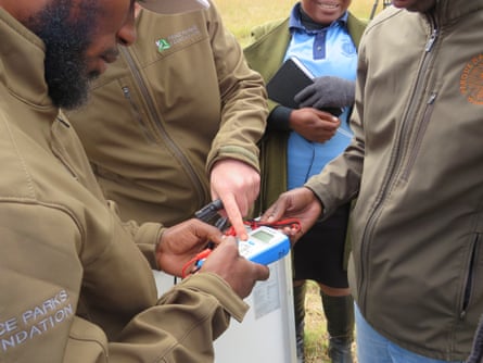 A group of people wearing khaki tops look at a handheld device