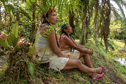 Two Indigenous women of the Amazon sit beside a river in traditional dress