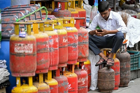 A man uses a mobile phone next to liquefied petroleum gas cylinders outside a shop in Bengaluru