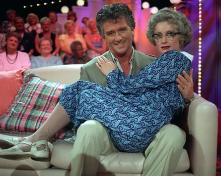 Carolie Aherne in the arms of Patrick Duffy on a sofa in front of a studio audience