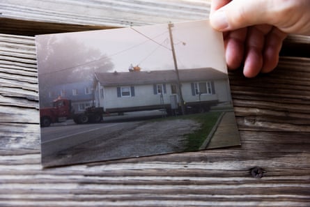 A hand holds a faded photograph of an old house against a wooden table