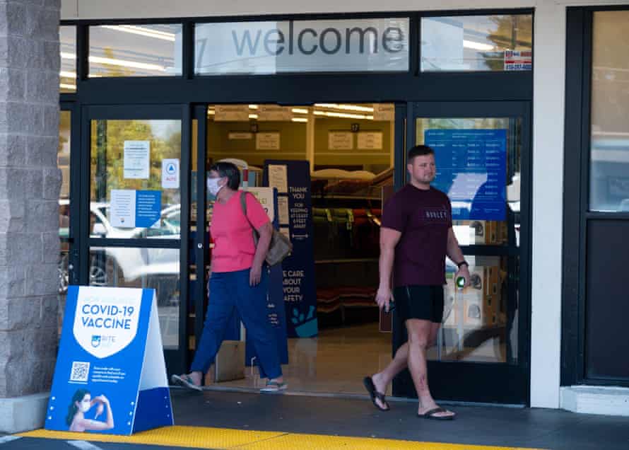 A woman wearing a mask and a man not wearing a mask exit a Rite Aid drug store in Sacramento.