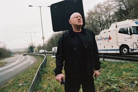Shaun Ryder stands on an embankment on a motorway