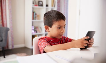 A boy aged four or five plays intently with a smartphone at a table at home