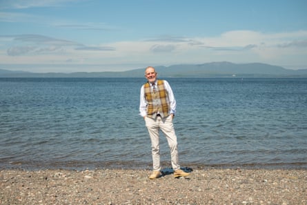 An older man in a tartan waistcoat stands on a beach
