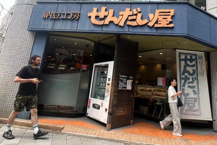 Two people walk past a restaurant adorned with letters from the Japanese alphabet.