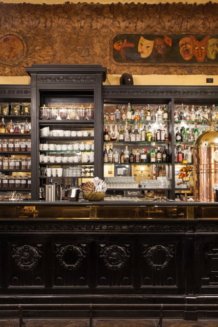 A dark wooden counter in a cafe, with shelves of cups and bottles behind it