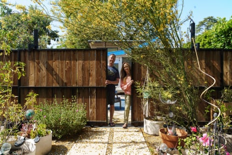 Man and woman stand in doorway of wooden fence looking into paved back garden