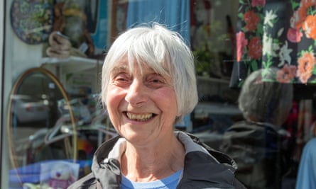 Mary Cullen: she has white hair in a straight bob and is smiling broadly in front of a shop window with patterned fabrics in the background.