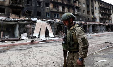 A Ukrainian serviceman in uniform walks past a row of shattered buildings