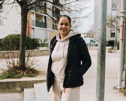 Farida Chater, smiling, stands on a street in a black puffer jacket, hands in pockets