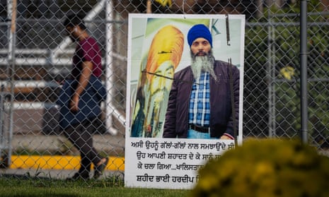 A poster of a man in a turban hangs on a chain-link fence as another man walks by.