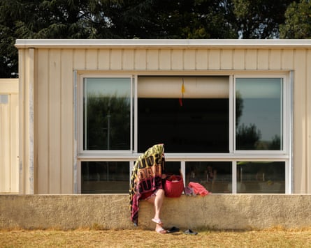 Person sat on wall with towel over head n front of small windowed building