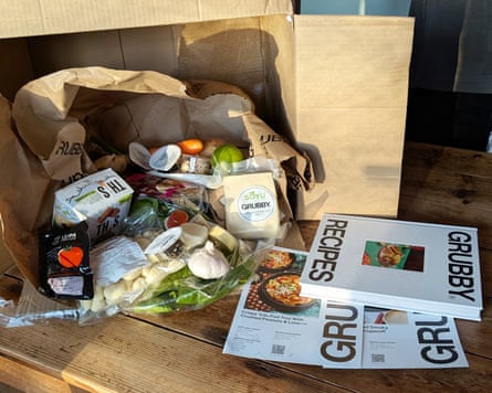 A Grubby recipe box contents of veg and protein with the Grubby recipe book and recipe cards on a table.