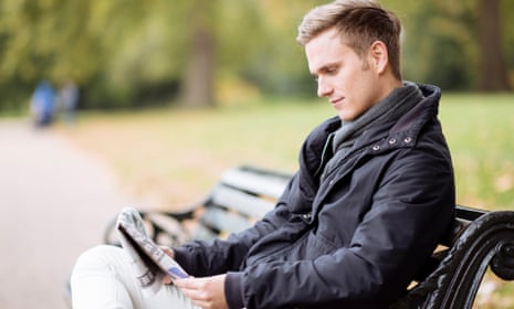 Young man sitting on bench reading newspaper