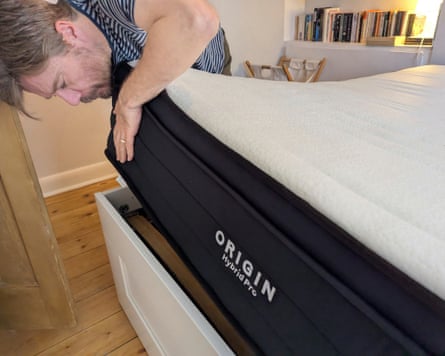 A man lifts up a mattress and looks underneath.