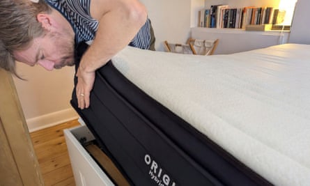 A man lifts up a mattress and looks underneath.