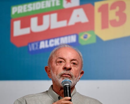 President Lula speaks on stage at a campaign rally in front of a poster that says President Lula 13