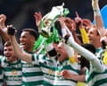 Celtic players celebrate together, one holding a trophy aloft, wearing green and white hooped jerseys