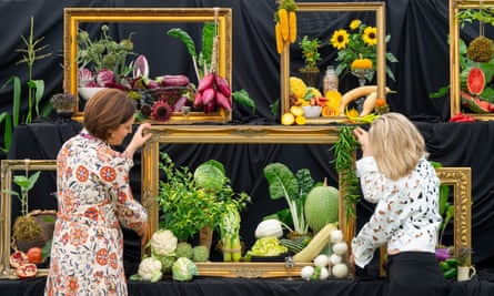 Two people move a picture frame around a display of vegetables